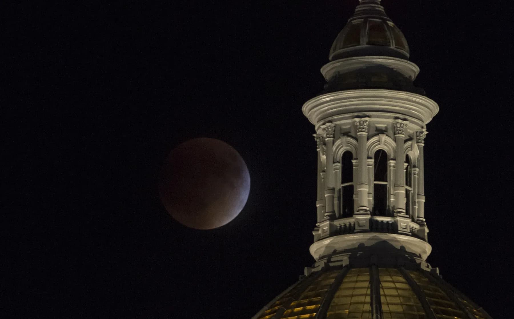A total lunar eclipse beside the gold dome of the Colorado State Capitol in Denver at night