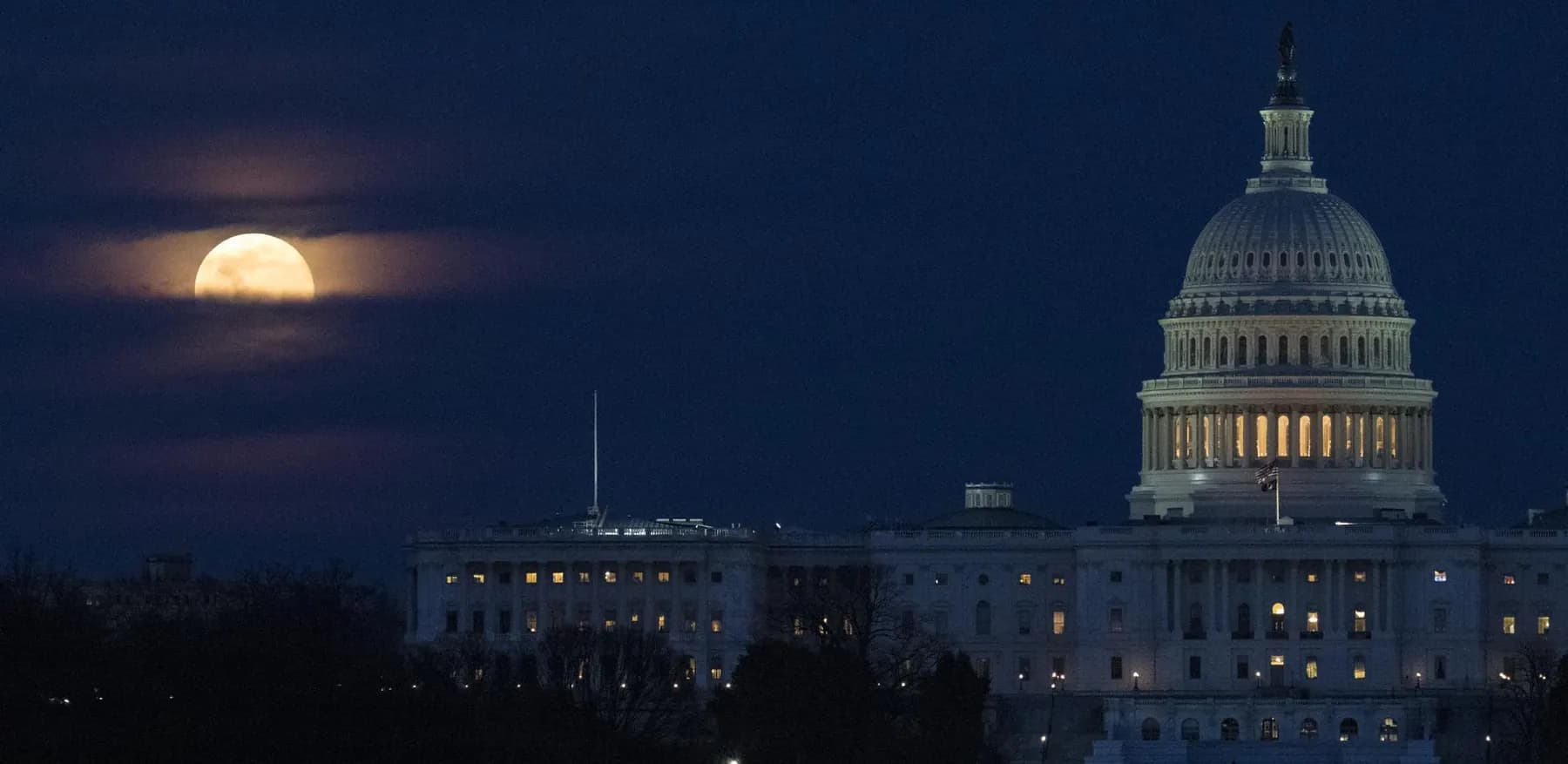 A supermoon rising through clouds behind the United States Capitol dome at dusk